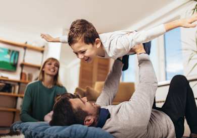 A man is lifting a child in the air while a woman watches.