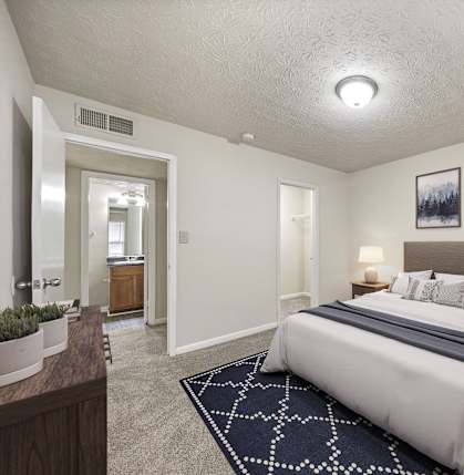 A bedroom with a large bed and a nightstand with a lamp at Bradford Gwinnett Apartments and Townhomes in Norcross, GA, 30071