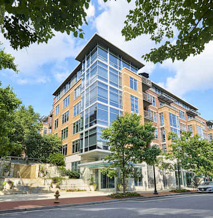 A modern building with a glass facade is surrounded by trees and has a stone staircase leading up to the entrance.