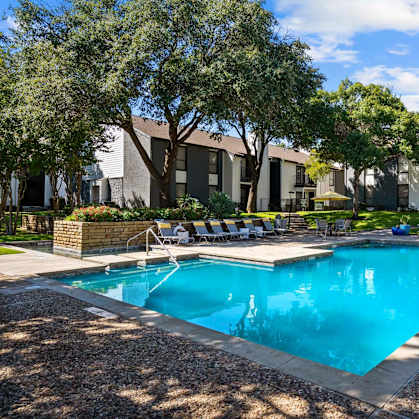 A swimming pool surrounded by trees and lounge chairs.