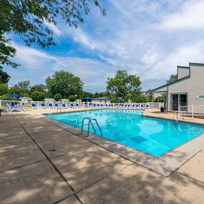 A large outdoor swimming pool with a diving board and a building in the background.