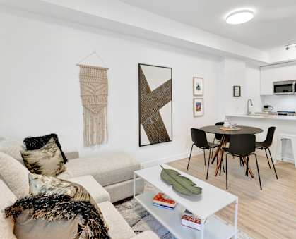 A modern living room with a white sofa, a coffee table, and a dining area in the background.