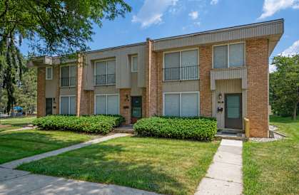 A brick apartment building with green bushes in front.