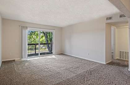 A spacious room with a carpeted floor and sliding glass doors leading to a balcony.