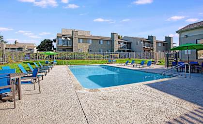A pool surrounded by chairs and a building in the background at The Henley Apartments, Suisun City, CA