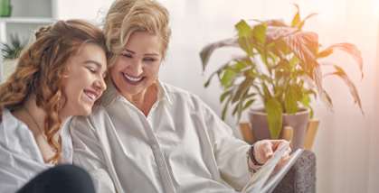 Two women are sitting on a couch, one is reading a book and the other is laughing.