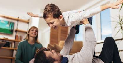 A man is lifting a child in the air while a woman watches.