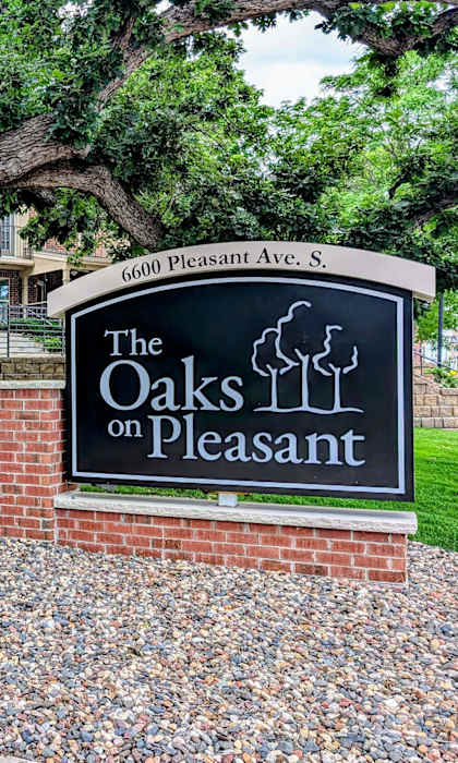 A sign for The Oaks on Pleasant is in front of a tree.