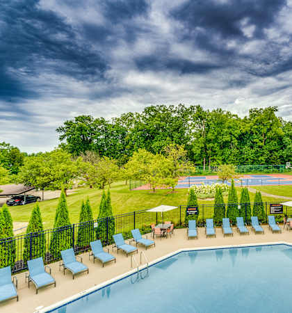 A large swimming pool surrounded by lawn chairs and trees.
