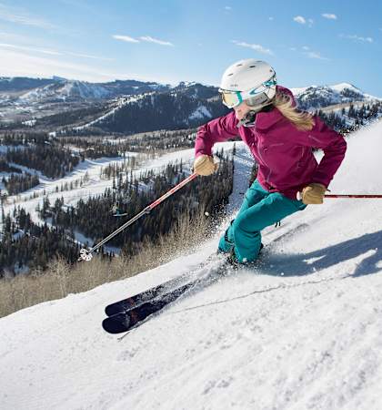A skier in a pink jacket and blue pants is skiing down a snowy mountain.