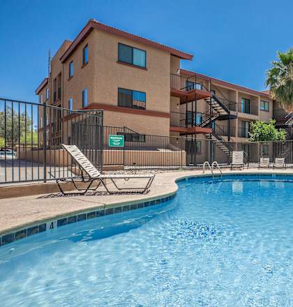 A swimming pool in front of a building with palm trees.