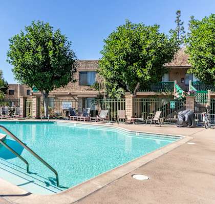 A swimming pool surrounded by trees and a building in the background. at Heritage Park, Rialto, CA