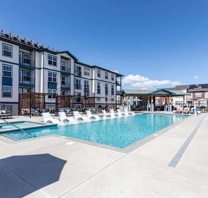 a swimming pool with lounge chairs around it in front of an apartment building