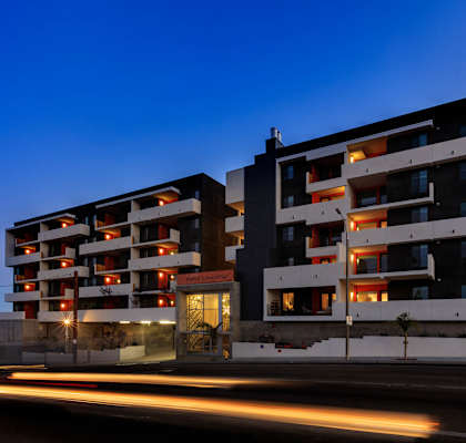 A modern apartment building with a dark facade and brightly lit windows.