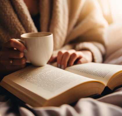 a woman reading a book and holding a cup of coffee at Amity Oak in Amityville, NY 11701