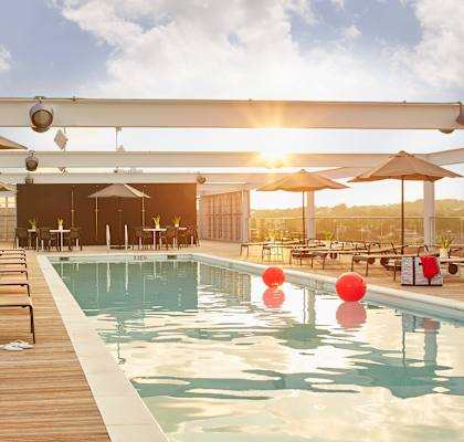 a swimming pool on the roof of a building with tables and umbrellas
