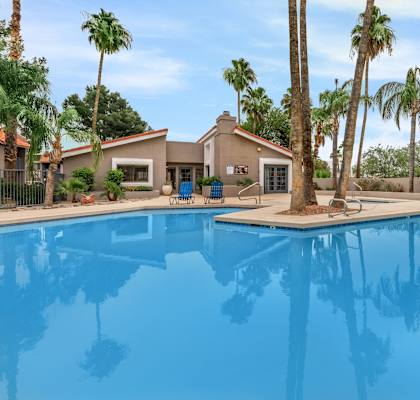 A pool in front of a house with palm trees.