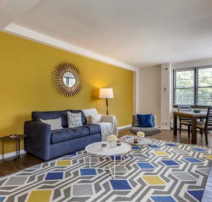 A living room with a blue couch, a white coffee table, and a flat screen TV mounted on the wall.