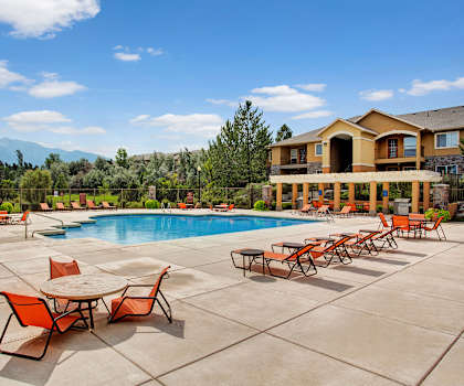 The turquoise outdoor pool with pool chairs, tables, and chairs with the apartments in the background at Legends at River Oaks Apartment Homes. 