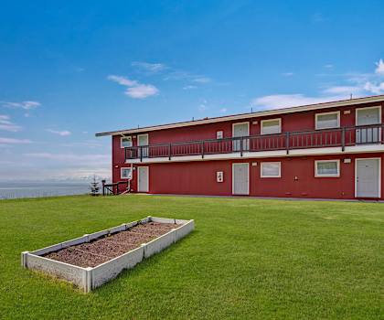 The exterior view at Bay Arms Apartments with a view of the water and the grassy area with a raised bed.  