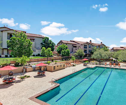 A turquoise outdoor pool surrounded by tables, chairs, and lounge chairs at Bela Rosa Apartments. 