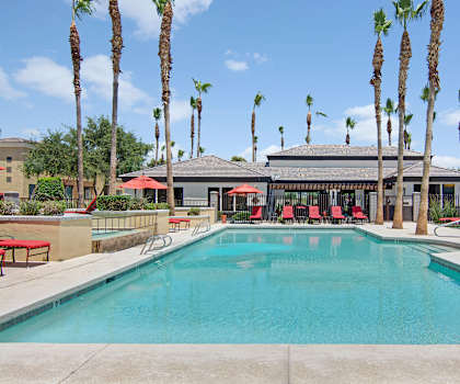 The turquoise outdoor pool with pool chairs, tables, and chairs with main office building in the background at Natura Villas Apartments. 