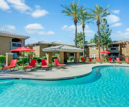 The turquoise outdoor pool with pool chairs, tables, and chairs with the apartments in the background at Reserve on the Arrowhead Apartment Homes. 