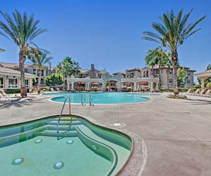 The turquoise outdoor pool with palm trees, pool chairs, tables, and chairs at Fresco Apartments. 
