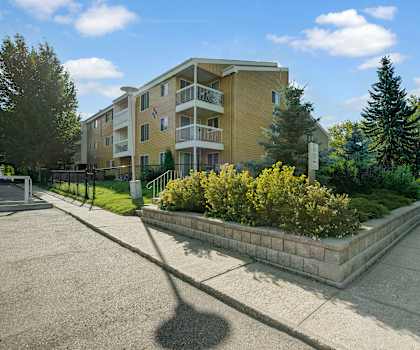 The exterior of the buildings and parking lot at surrounded by trees, bushes, and green spaces at Gateway Gardens. 
