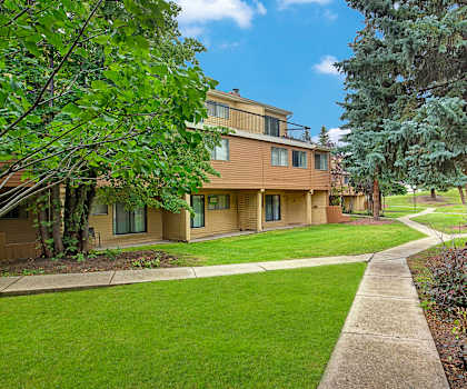 The exterior of the apartments and the green space with walkways, grass, trees, and shrubs at Lakewood Heights. 