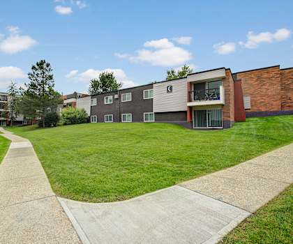 The pathway surrounded by grass and trees leading to the apartment building at Park Place South Apartments. 