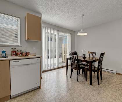 The cozy dining room with a dining table and chairs and a view of the kitchen with light counters, light cabinets, and white appliances at Ridgeview Village Apartment Homes. 