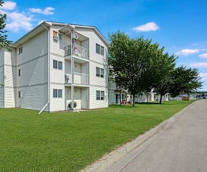 The exterior of the white apartment buildings surrounded by beautiful grass and trees at Sol Terrace Apartment Homes. 