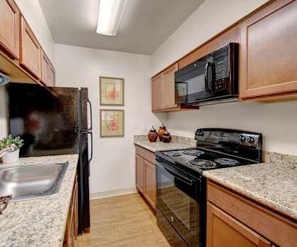 A kitchen with wooden cabinets and marble countertops at Copper Stone Apartments. 