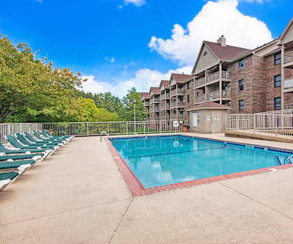The large, turquoise outdoor pool with pool chairs, tables, and chairs with the apartments in the background at Town Centre Apartment Homes. 
