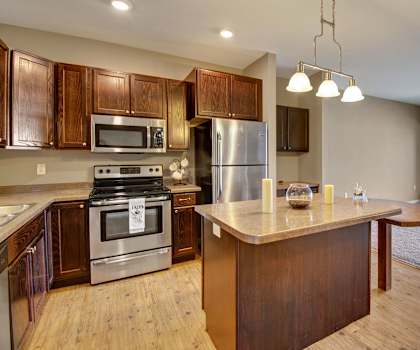A kitchen with stainless steel appliances and wooden cabinets at Dakota Common Apartments. 