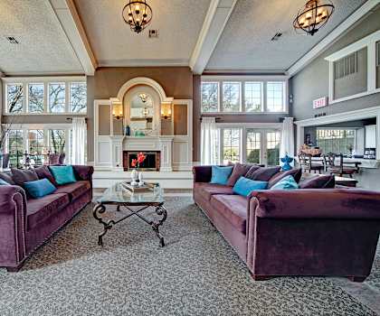 The resident lounge with a fireplace, piano, couches, plush chairs, and coffee tables at Brookwood Village Apartments.