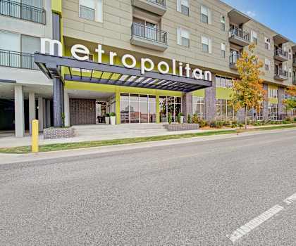 The street view of the Metropolitan with trees and grassy areas on the sidewalk, and a large sign displaying the name of the apartment building. 