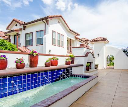 A white and blue fountain with potted plants on top, surrounded by white buildings at Andalucia Villas. 