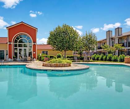 The turquoise outdoor pool with pool chairs, tables, and chairs with the apartments in the background at High Plains. 