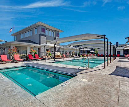 The turquoise outdoor pool with pool chairs, tables, and chairs with the apartments in the background at Le Mirage Apartments.