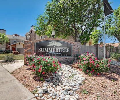 The exterior sign with trees and surrounded by greenery, trees, and flowers with the buildings in the background of Summertree Place Residences. 