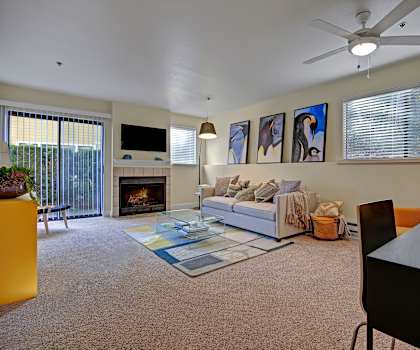 The living room with a couch, coffee table, decorations including penguin artwork, a TV, and door to the patio at Foster Greens Apartments. 