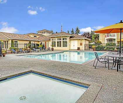 The turquoise outdoor pool with pool chairs, tables, and chairs with the apartments in the background at Lakeside Apartments. 