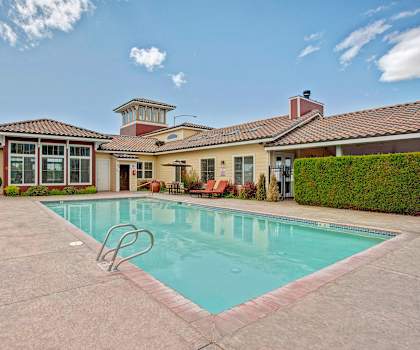 The large, turquoise outdoor pool with pool chairs, tables, and chairs with the apartments in the background at the Vintage Apartment Homes. 