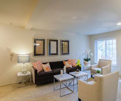 The spacious living room with a couch, throw pillows, wall art, plush chairs, coffee table, decorations, a TV, and windows at Windsong Apartment Homes. 