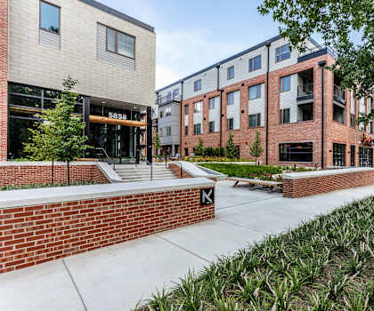 a sidewalk in front of a brick building with trees and plants