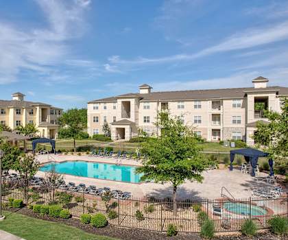 A large apartment complex with a pool and a fenced in area with trees.