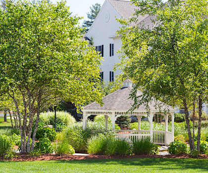 a white gazebo in a park with a house in the background