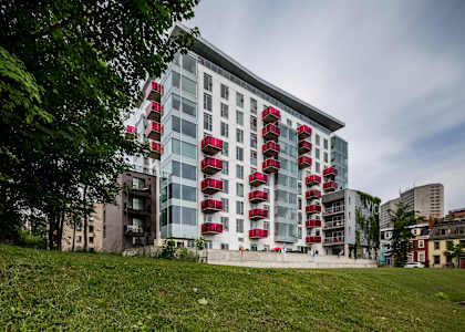 A modern building with red balconies is surrounded by greenery.